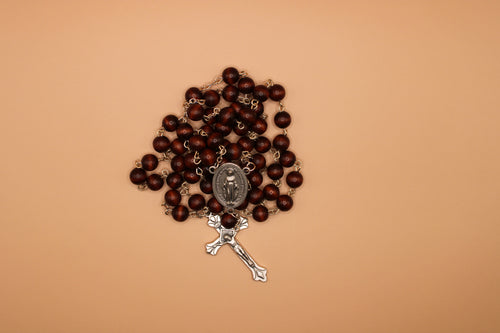 Brown rosary with silver crucifix on a beige background