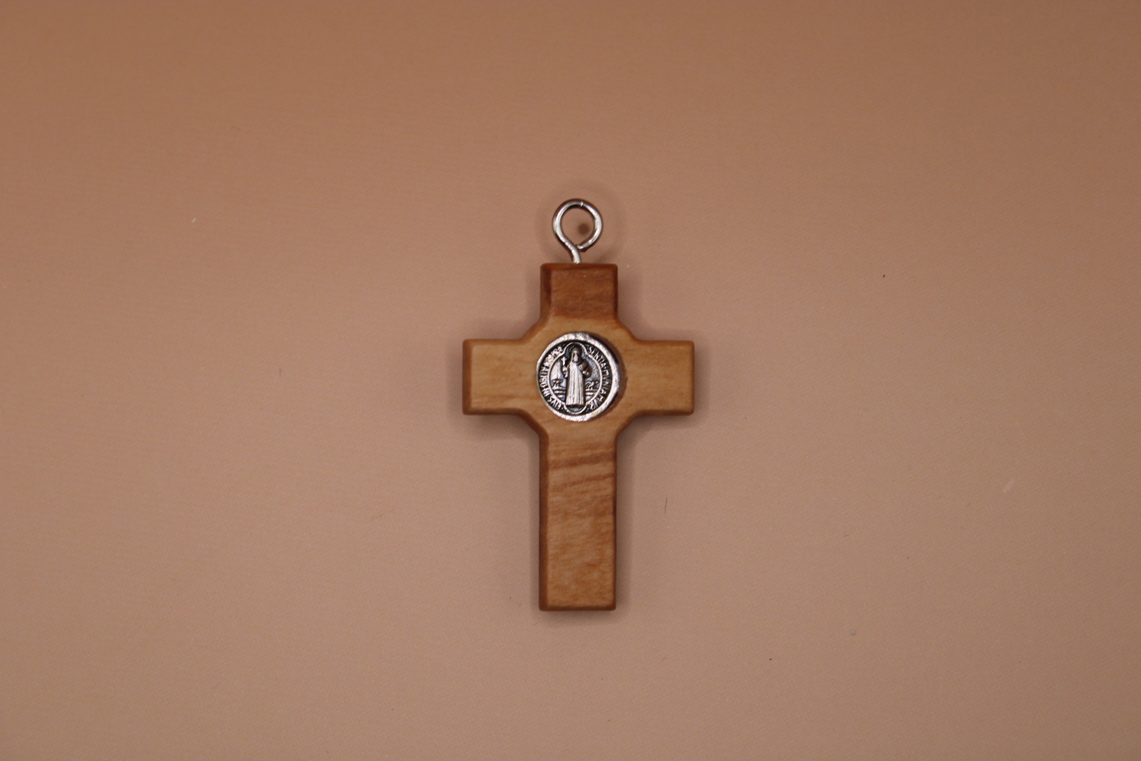 Wooden cross pendant with a St. Benedict seal on a beige background
