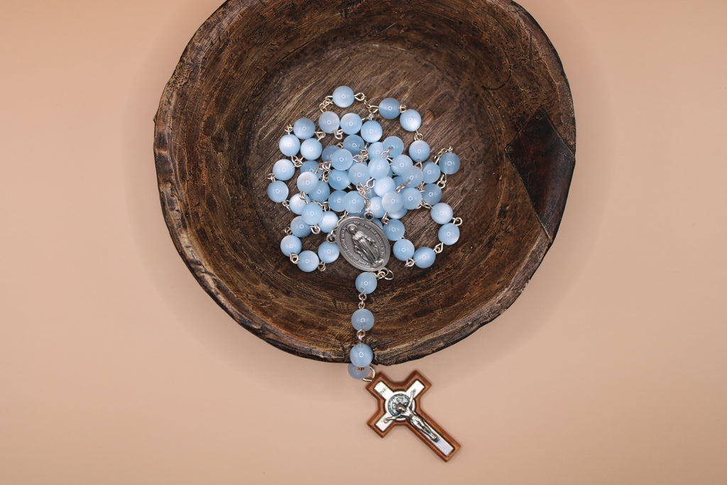 Blue rosary in a wooden bowl on a beige background