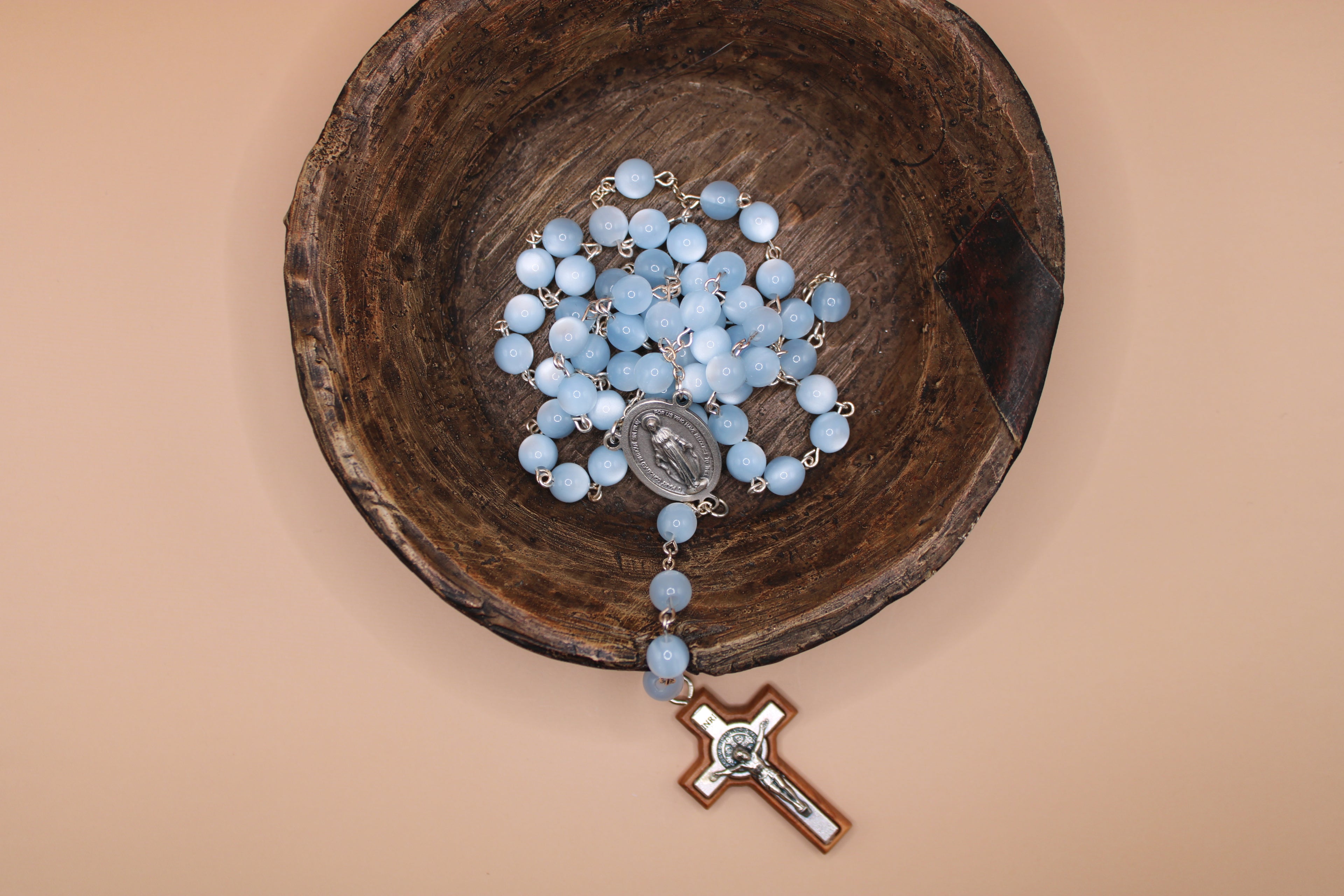 Blue rosary in a wooden bowl on a beige background