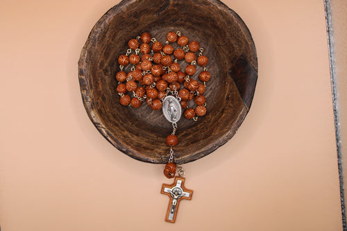 Wooden rosary with a cross pendant in a wooden bowl on a beige background