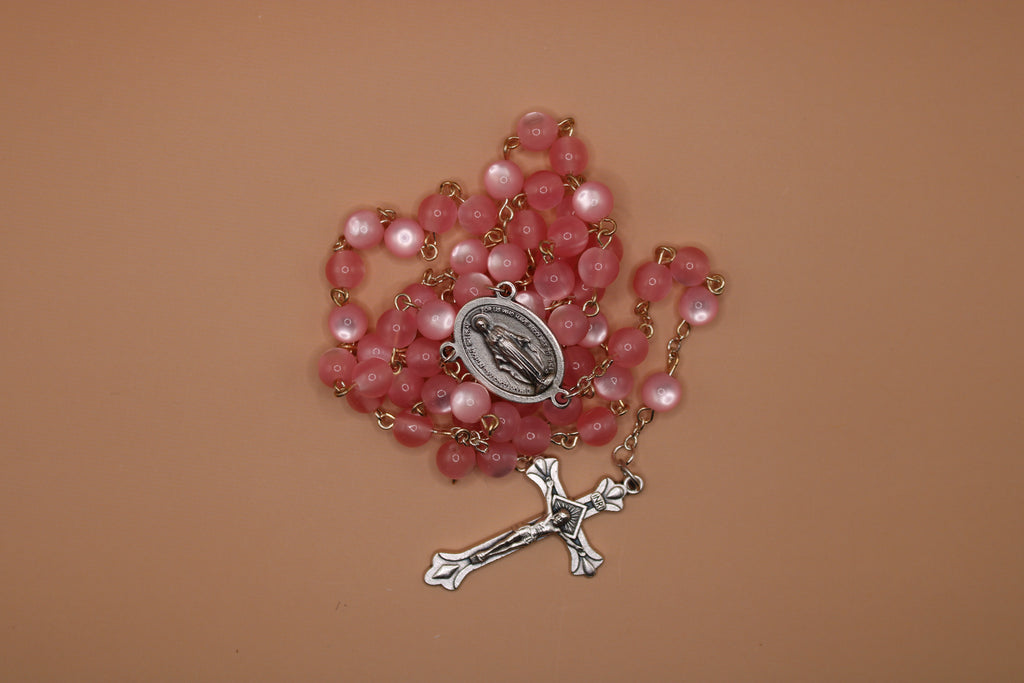 Pink rosary with a silver cross and medal on a brown background