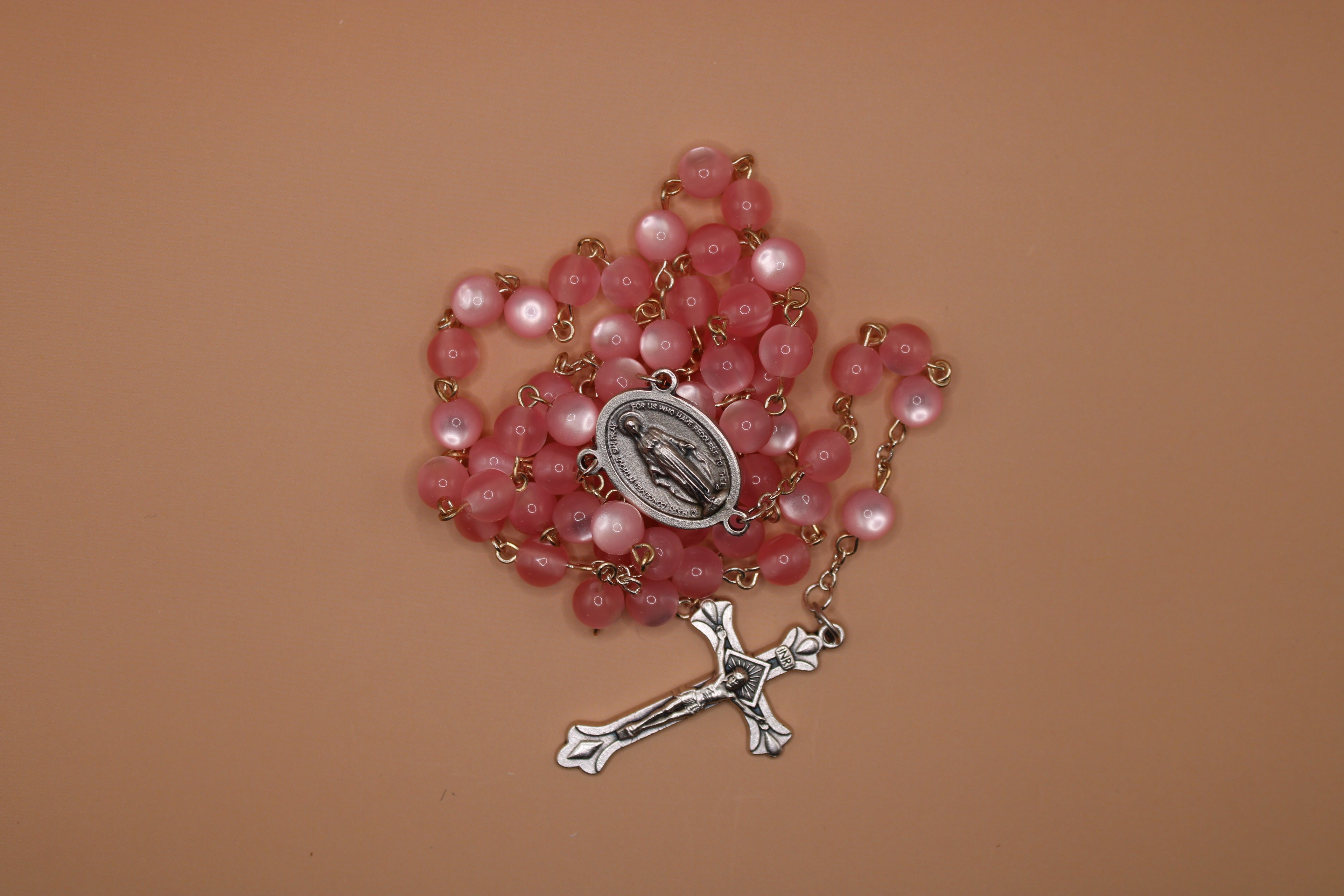 Pink rosary with a silver cross and medal on a brown background